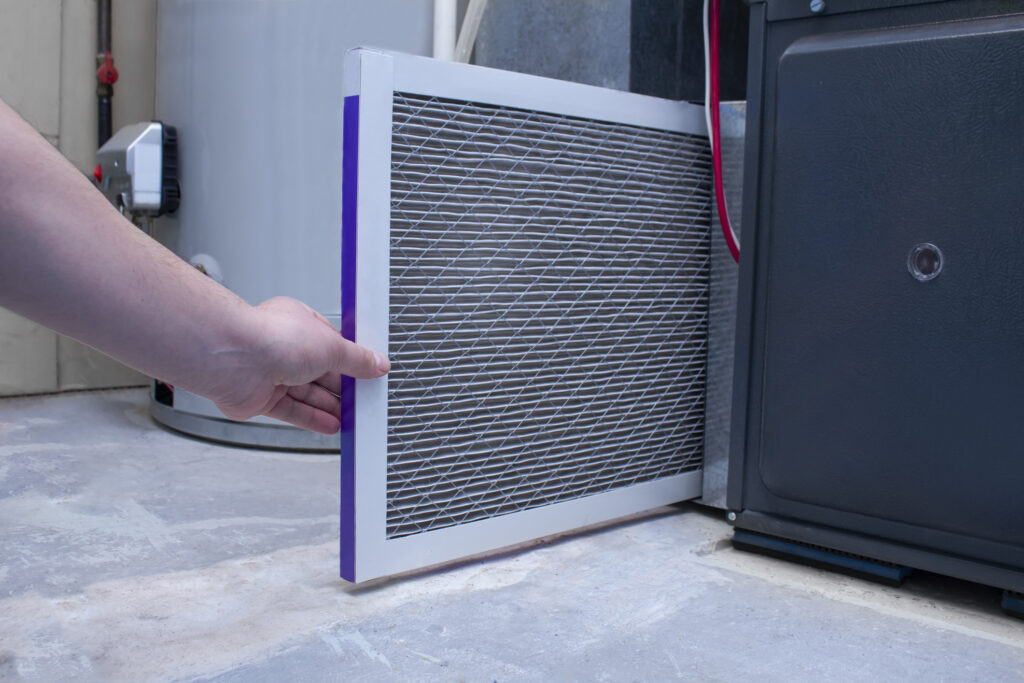 Hand pulling a clogged furnace filter from the unit.